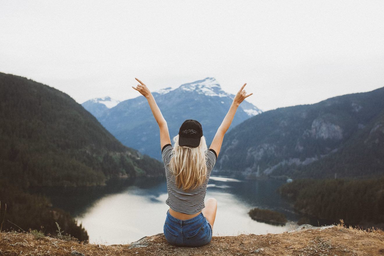 hero banner image. Woman sitting on cliff cheering